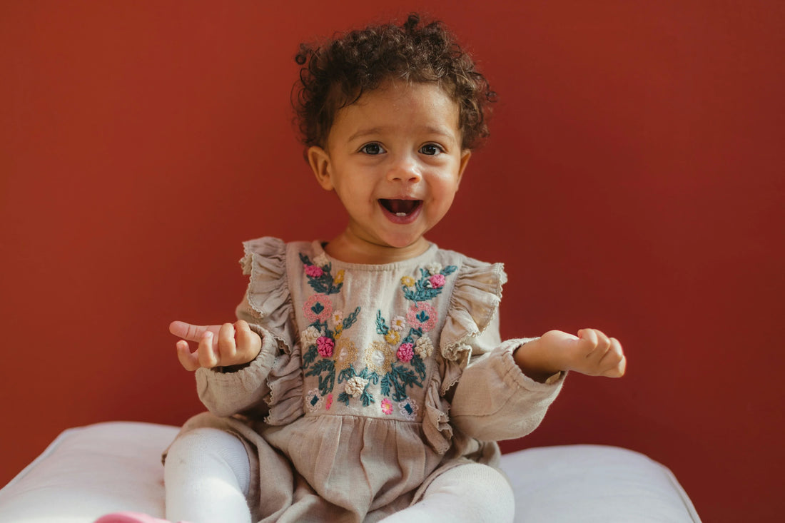 Happy baby girl in embroidered floral dress against red wall