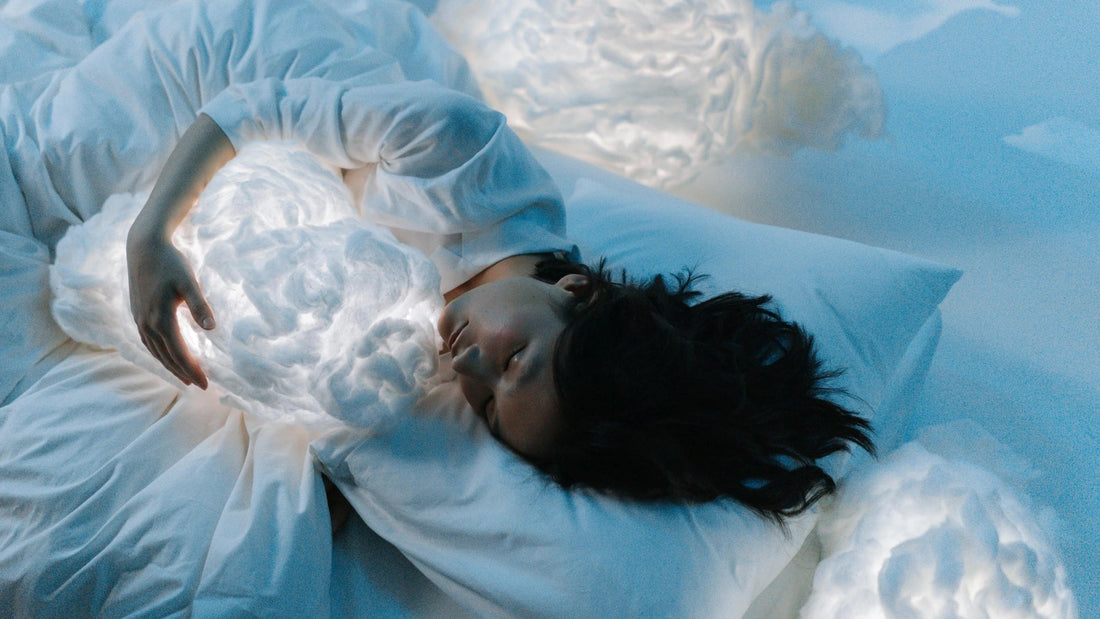 Woman sleeping in bed with glowing cloud-shaped pillows, dreamy blue bedroom