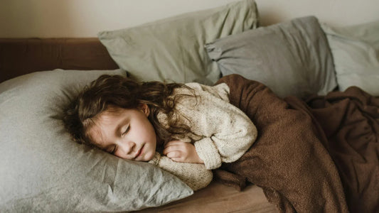 Little girl sleeping peacefully on a couch with a brown blanket.