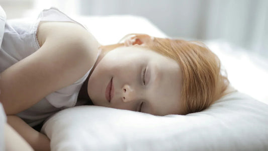 Peaceful red-haired little girl sleeping on a white pillow in bright bedroom.