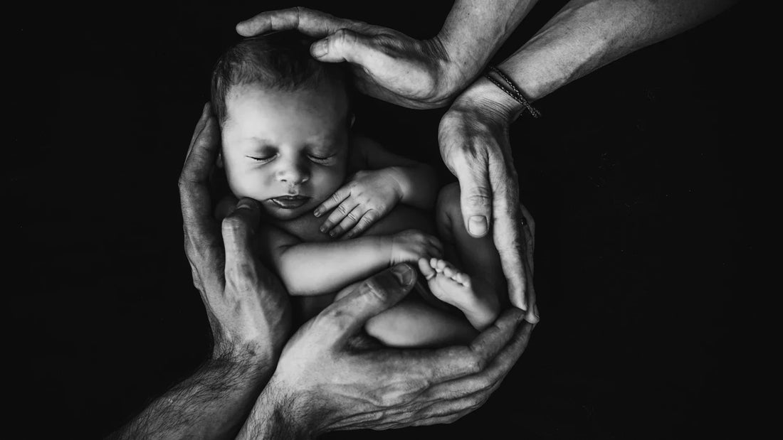 Black and white photo of newborn baby held gently in parents' hands.