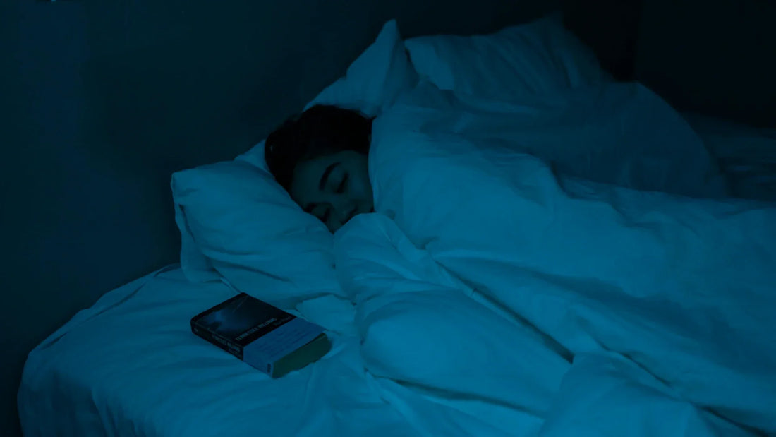 Woman sleeping in a dimly lit blue bedroom with a book on the bed.