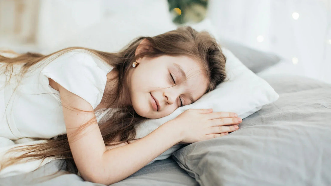Little girl sleeping soundly on grey bedding with white pillow.