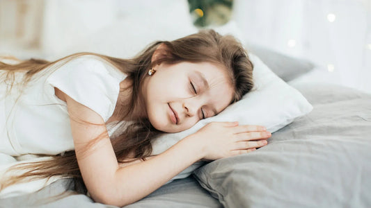 Little girl sleeping soundly on grey bedding with white pillow.