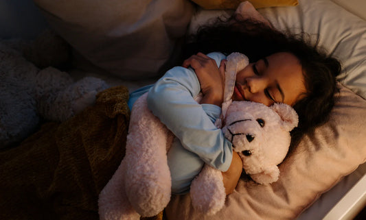 Little girl sleeping while hugging a fluffy pink teddy bear at bedtime.