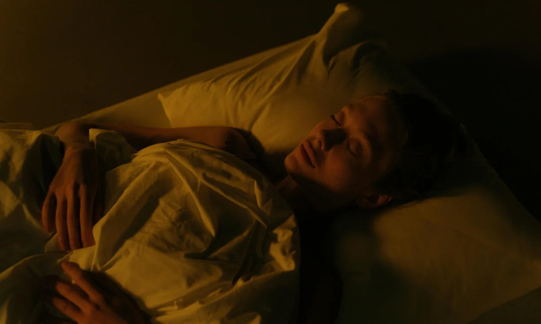 Woman sleeping peacefully in warm dim night lighting with white bed sheets.