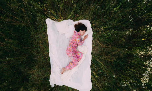 Top down view of woman in pink floral pajamas sleeping on white bedding amid wild meadow flowers.
