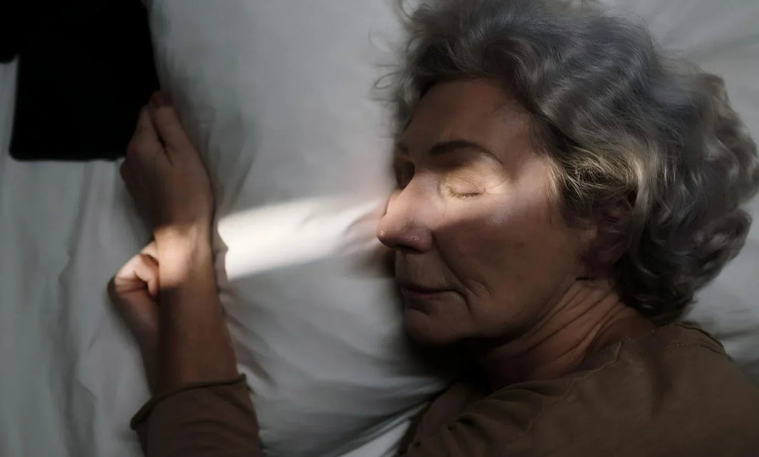 Elderly woman lying awake in bed at night, tense facial expression showing senior insomnia and nighttime anxiety — visual illustration of age-related poor sleep quality, shallow sleep and sleep disturbance in older adults.