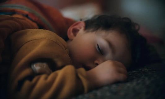 Close-up shot of curly-haired toddler napping peacefully on soft fabric surface, dim warm tone scene for gentle kids rest sleep aid.